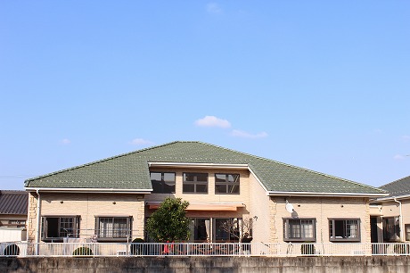 介護施設の建物外観。白とグリーンの二色屋根、平屋建て、手摺付きウッドデッキ付き。